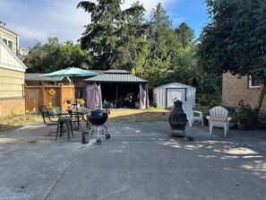 Un patio trasero con una parrilla, mobiliario exterior, un cobertizo y un porche cubierto.