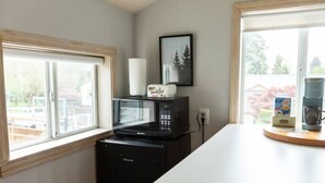 A compact kitchen with a microwave and toaster on a counter, a window with a view of the outdoors, and a framed picture on the wall.