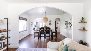 A spacious living room with a white sofa, a coffee table, and a dining area with wooden chairs and a table.