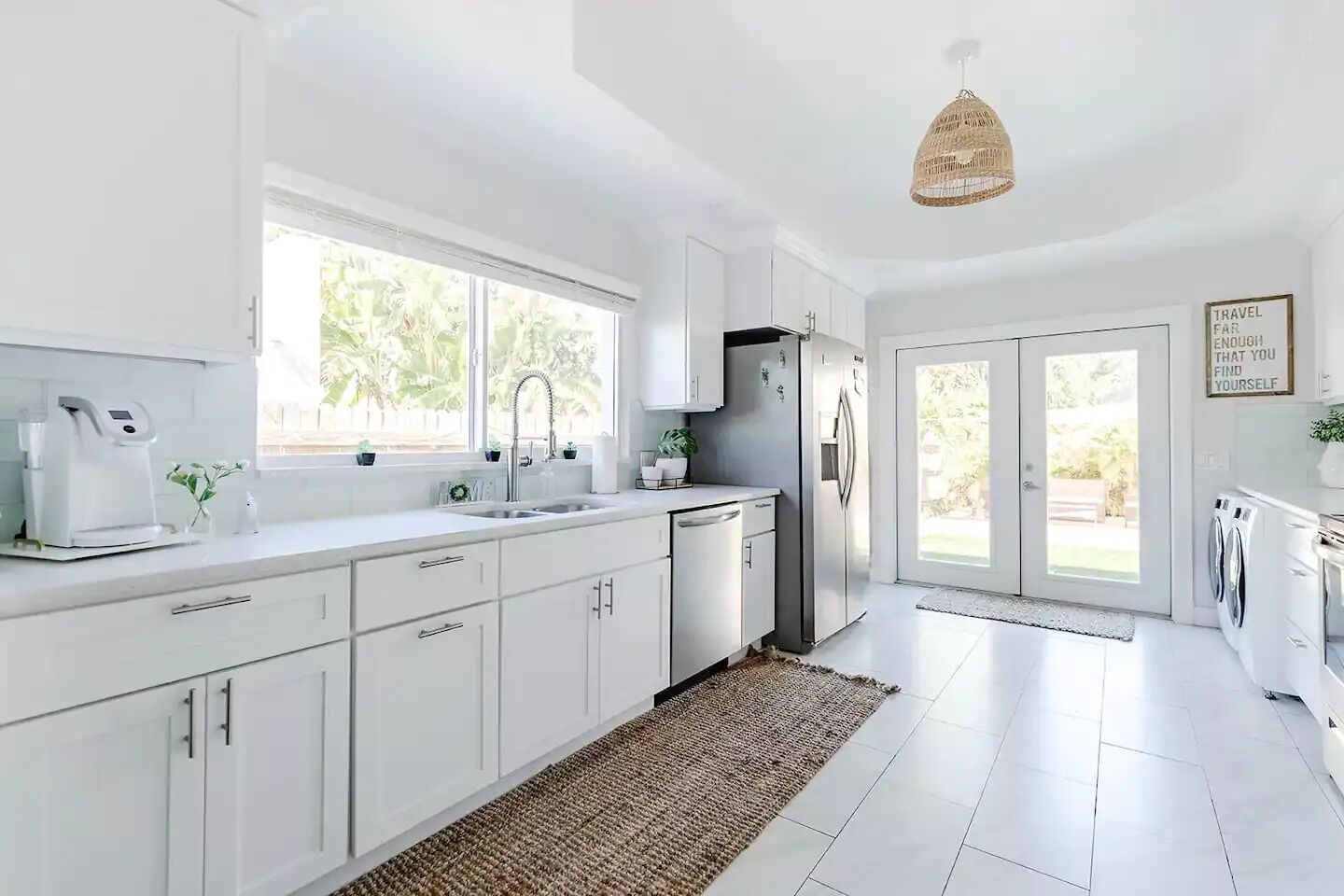A modern kitchen with white cabinetry, a stainless steel refrigerator, a coffee maker, and a large window providing natural light.
