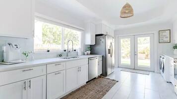 A modern kitchen with white cabinetry, a stainless steel refrigerator, a coffee maker, and a large window providing natural light.