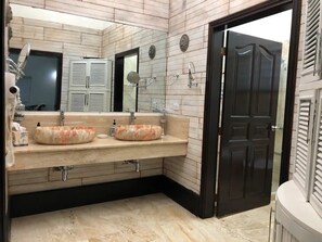 Casa de banho com duas pias ovais, um espelho grande e uma porta escura.