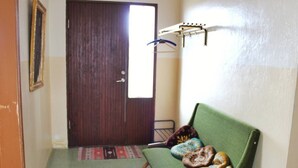 A room with a green sofa, a wooden door, a hanging coat rack, and a patterned rug. - Old Authentic Icelandic Farmhouse (Fossholl Thingeyjarsveit)