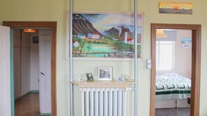 A bedroom with a bed, a radiator, a shelf with pictures, and a painting on the wall. - Old Authentic Icelandic Farmhouse (Fossholl Thingeyjarsveit)