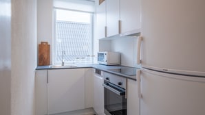 A compact kitchen with white cabinets, a microwave, a refrigerator, and a window with blinds. - 1 Bed Apartment Sleeps 2 with Parking, WiFi, Tv (Aalborg)