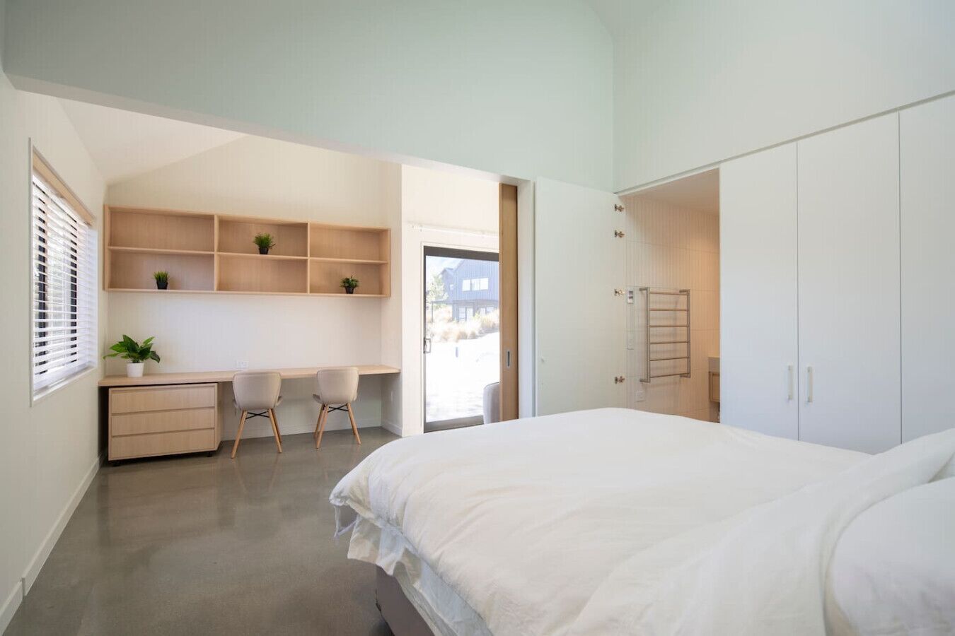Une chambre moderne avec un grand lit, un bureau avec des chaises et des étagères intégrées.