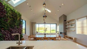 A modern kitchen with a large island, a dining area with a view of the outdoors, and a living area with a fireplace and shelves.