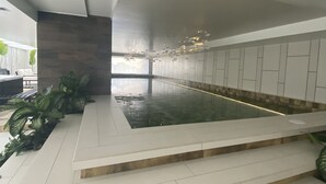 A modern indoor swimming pool with a minimalist design, featuring a long, narrow pool, a stone accent wall, and a series of steps leading into the water. - Hermosa Suite en la Carolina. Choita Hospedajes (Quito)