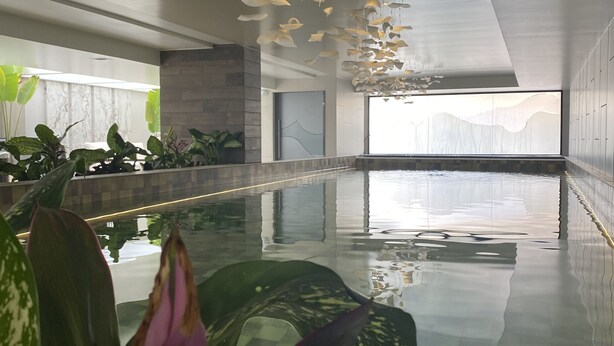 A modern indoor pool area with a glass floor, large potted plants, and a view of the city skyline through large windows. - Hermosa Suite en la Carolina. Choita Hospedajes (Quito)