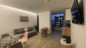 A modern living room with a grey sofa, a glass dining table, and a TV mounted on the wall. - Hermosa Suite en la Carolina. Choita Hospedajes (Quito)