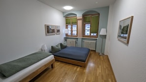 A bedroom with a bed, a bench, two windows with blinds, a radiator, and framed pictures on the wall. - Holiday Apartment "Am Markt" with Wi-Fi (Weimar)