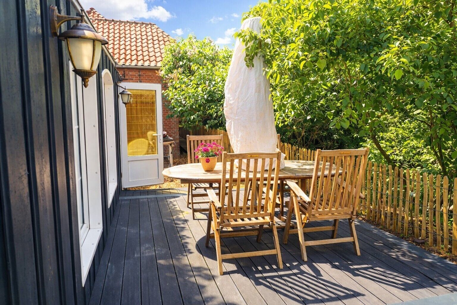 A wooden deck with a table and chairs, a potted plant, and a white umbrella.