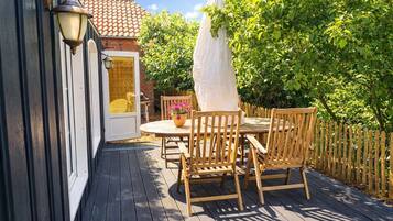 A wooden deck with a table and chairs, a potted plant, and a white umbrella.