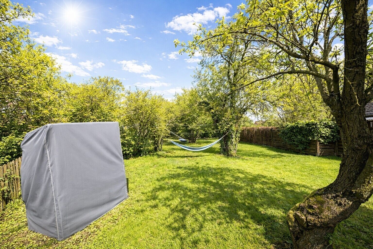 A backyard with a hammock, a covered object, and a tree.