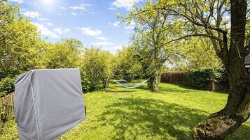 A backyard with a hammock, a covered object, and a tree.