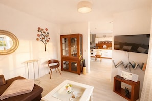 Un salon comprenant un canapé, une table basse avec un vase, un meuble en bois et un téléviseur fixé au mur.