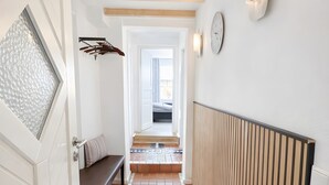 Un pasillo con suelo de baldosas, un banco, un reloj en la pared y una puerta con panel de vidrio esmerilado.