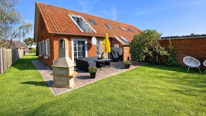 Una casa con techo inclinado, un patio con mobiliario exterior y un muro de ladrillo.