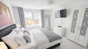 Un dormitorio moderno con cama, mesita de noche, televisor, armario y ventana con cortinas.
