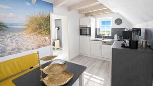A modern kitchen with a view of the beach, a dining area with a yellow chair, and a window with a view.