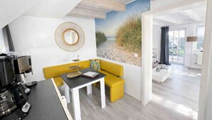A modern room with a yellow sofa, a coffee machine, a table, and a beach mural.