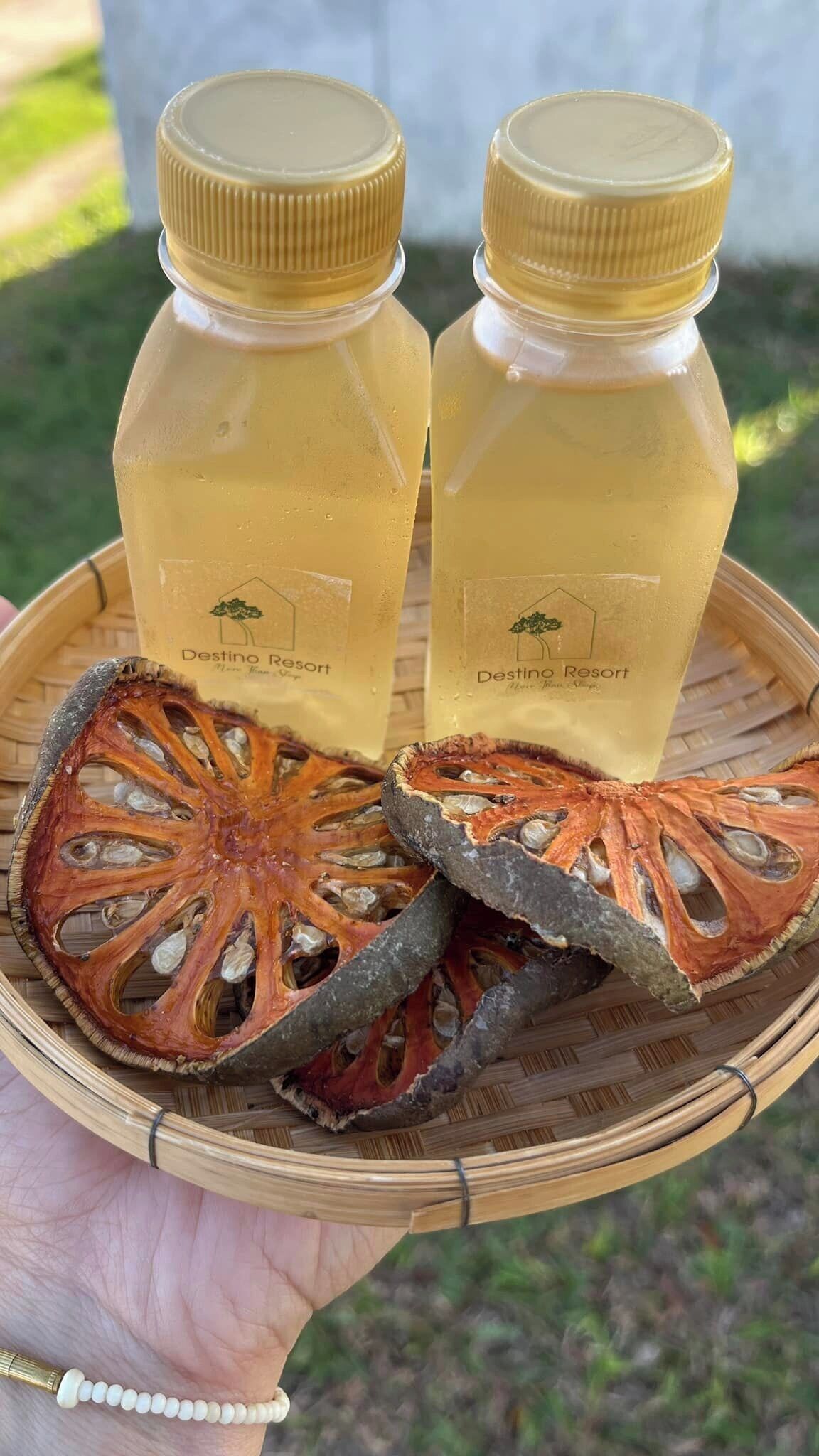 Duas garrafas de líquido amarelo com etiquetas, colocadas em um tabuleiro de tecido com frutas secas fatiadas.