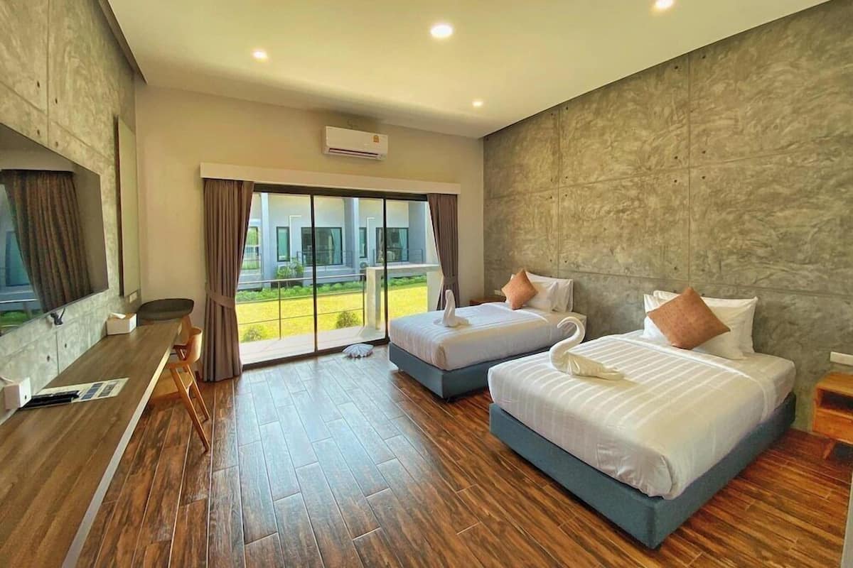 A hotel room with two beds, a wooden floor, a large window, and a view of greenery.