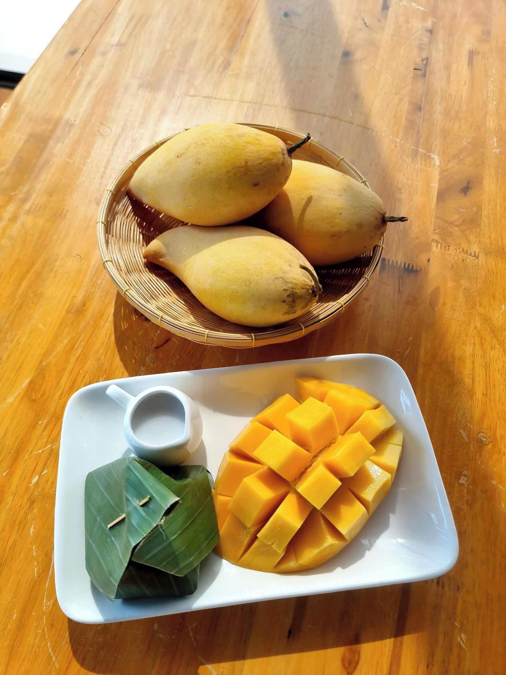 A plate with sliced mango and a bowl of bananas on a wooden table.
