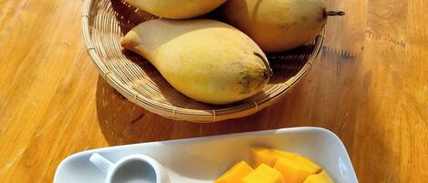 A plate with sliced mango and a bowl of bananas on a wooden table.