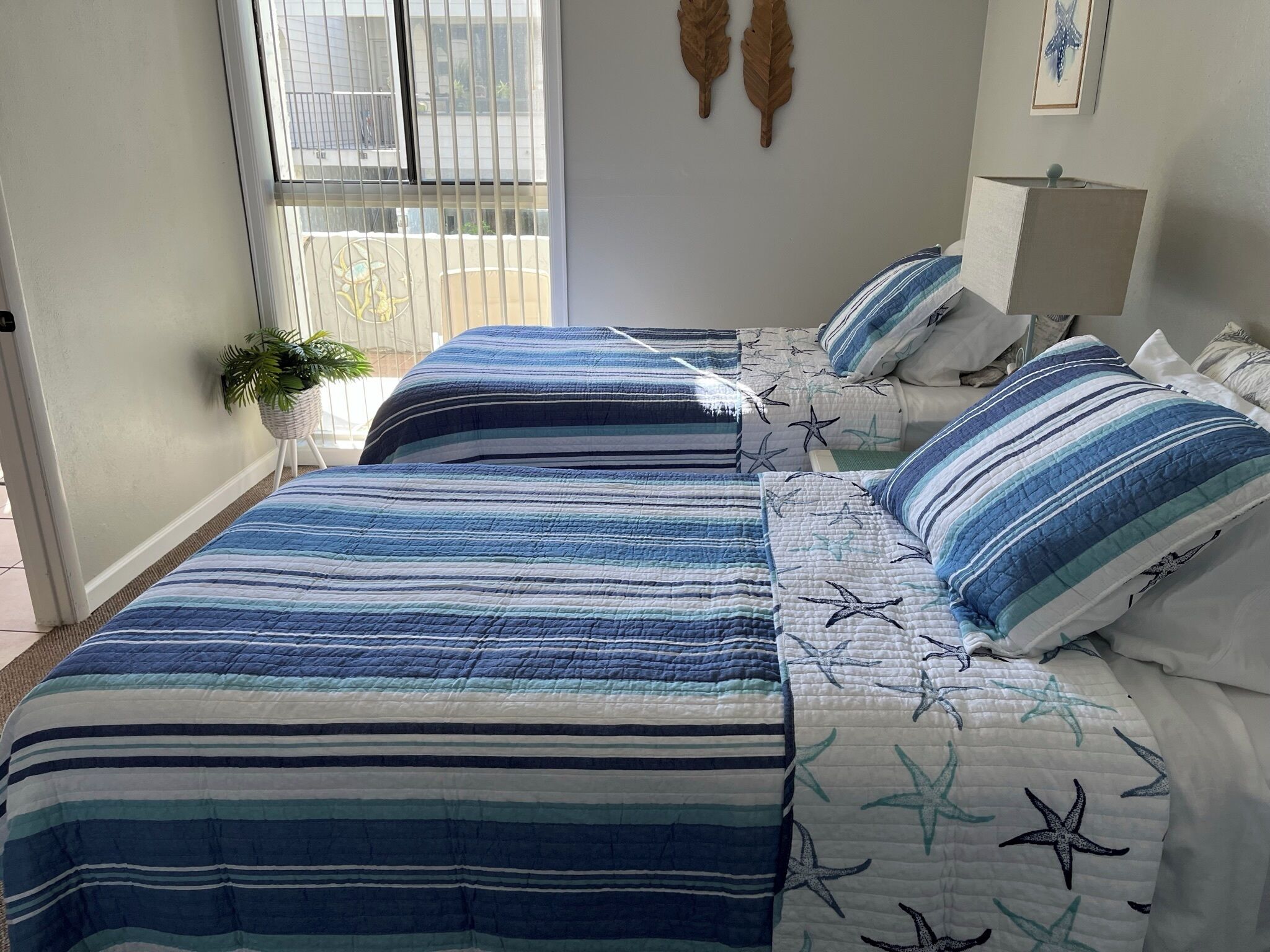 Ein Schlafzimmer mit zwei Betten, gestreifter Bettwäsche, Sternmuster, einer Topfpflanze und einem Fenster mit Jalousien.