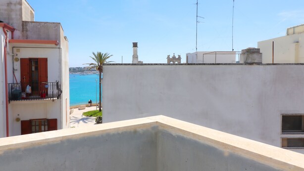 A balcony with a view of the sea, a building with a red door, and a white wall. - Azzurra's House Near the sea in Otranto (Otranto)