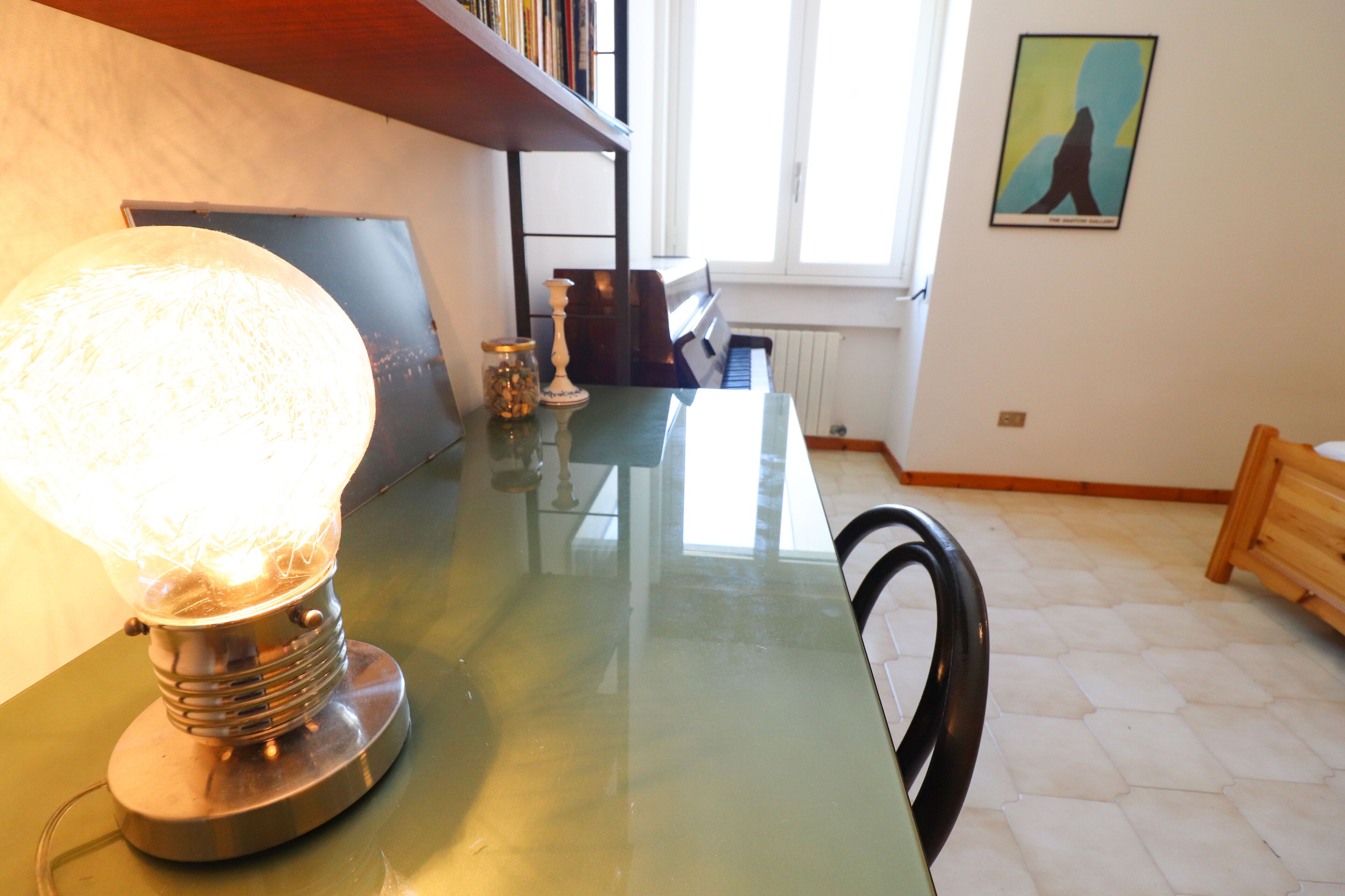 A room with a piano, a table with a lamp, and a painting on the wall.
