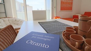 A modern living room with a white sofa, a dining table with a blue book titled "Il Grande Salento per immagini," and a set of terracotta cups. - Azzurra's House Near the sea in Otranto (Otranto)