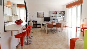 A modern kitchen with a white countertop, red bar stools, and a dining area with a white table and chairs. - Azzurra's House Near the sea in Otranto (Otranto)