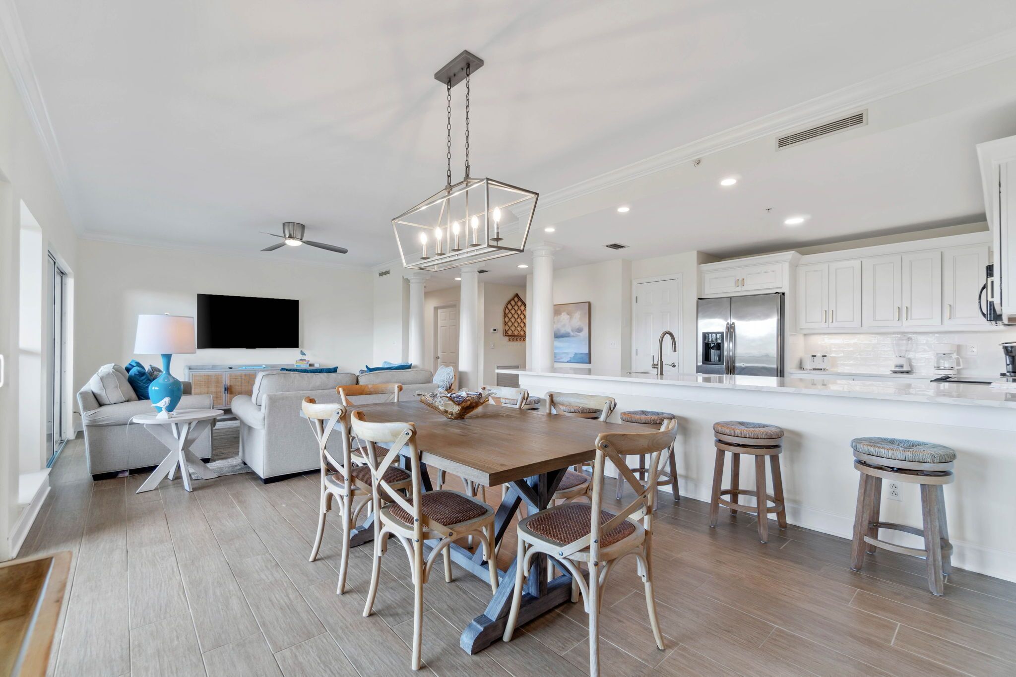 A modern kitchen with white cabinets, a central island, and a dining area with a wooden table and wicker chairs.