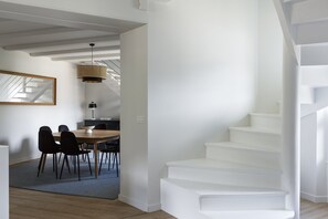 Un intérieur moderne avec un escalier, un coin repas comprenant des chaises et une table, et une cuisine en arrière-plan.
