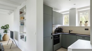 Uma cozinha moderna com armários cinza, bancada branca e janela com vista para árvores.