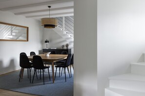 Un espace de salle à manger moderne avec une table en bois et des chaises noires, un luminaire suspendu et un escalier en arrière-plan.