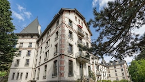 Um edifício de vários andares com arquitetura clássica, com varandas e uma escadaria que leva à entrada.