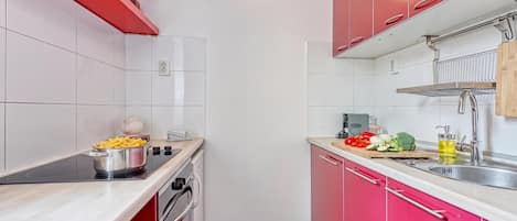 Una cocina pequeña con armarios rojos, estufa y fregadero.