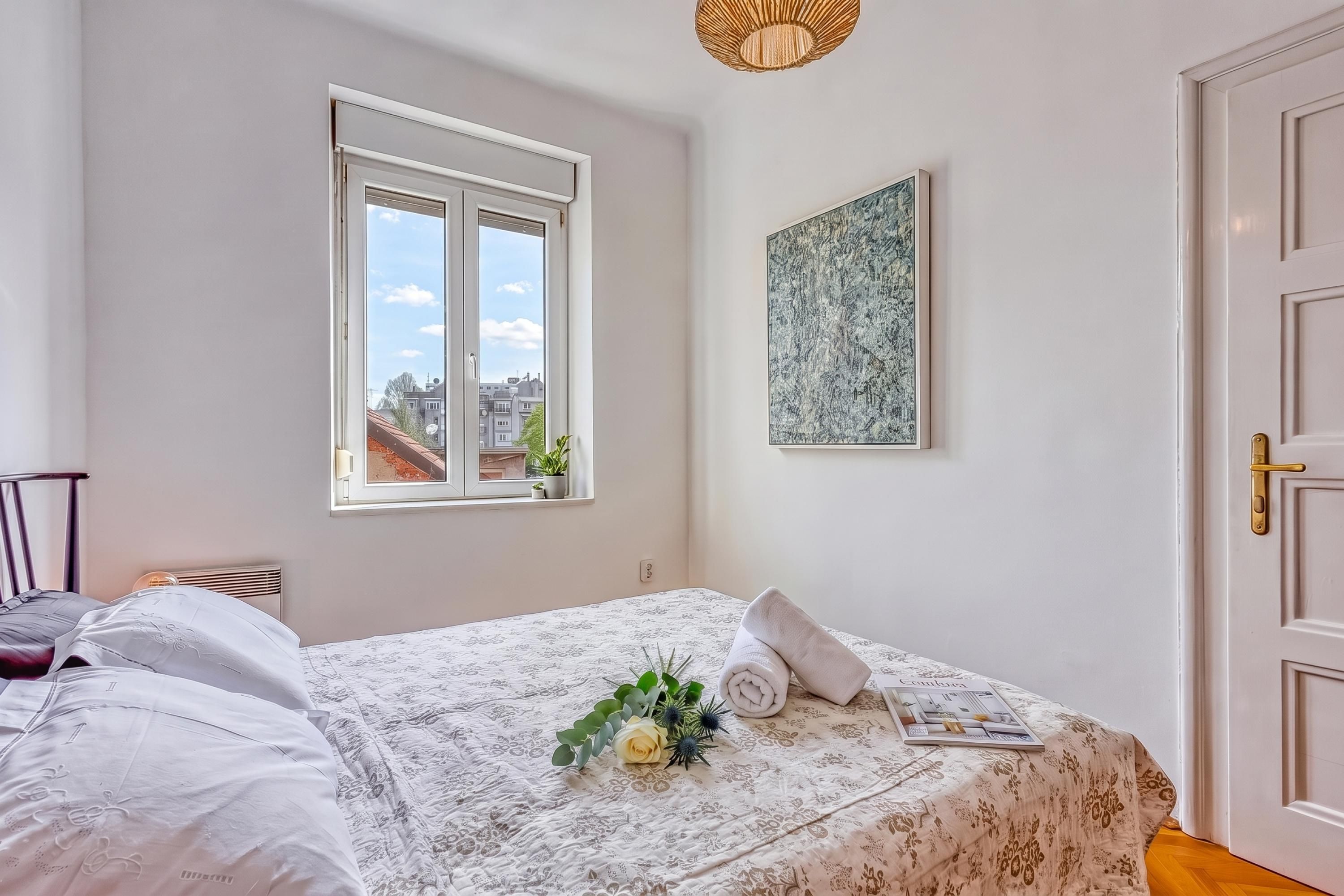 Un dormitorio con una cama, una ventana, una puerta y una obra de arte colgada en la pared.