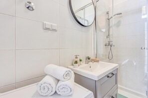 Een moderne badkamer met een wit wastafelmeubel, een spiegel, een douchecabine van glas en netjes opgerolde handdoeken op het aanrecht.
