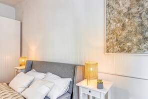 A hotel room with a bed, bedside tables, a lamp, and a wall-mounted artwork.