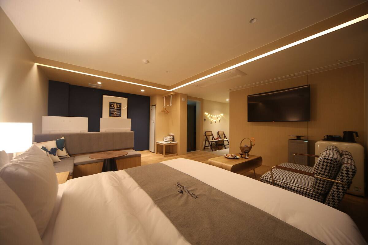 A modern hotel room with a large bed, a sofa, a TV, and a desk.