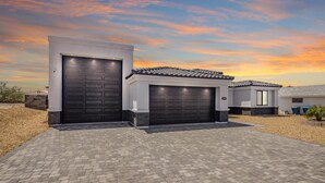 Ett modernt hus med två garageportar, en asfalterad uppfart och en klar himmel.