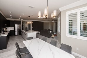 Une cuisine moderne dotée d’un îlot en marbre, d’appareils électroménagers en acier inoxydable et de luminaires suspendus.