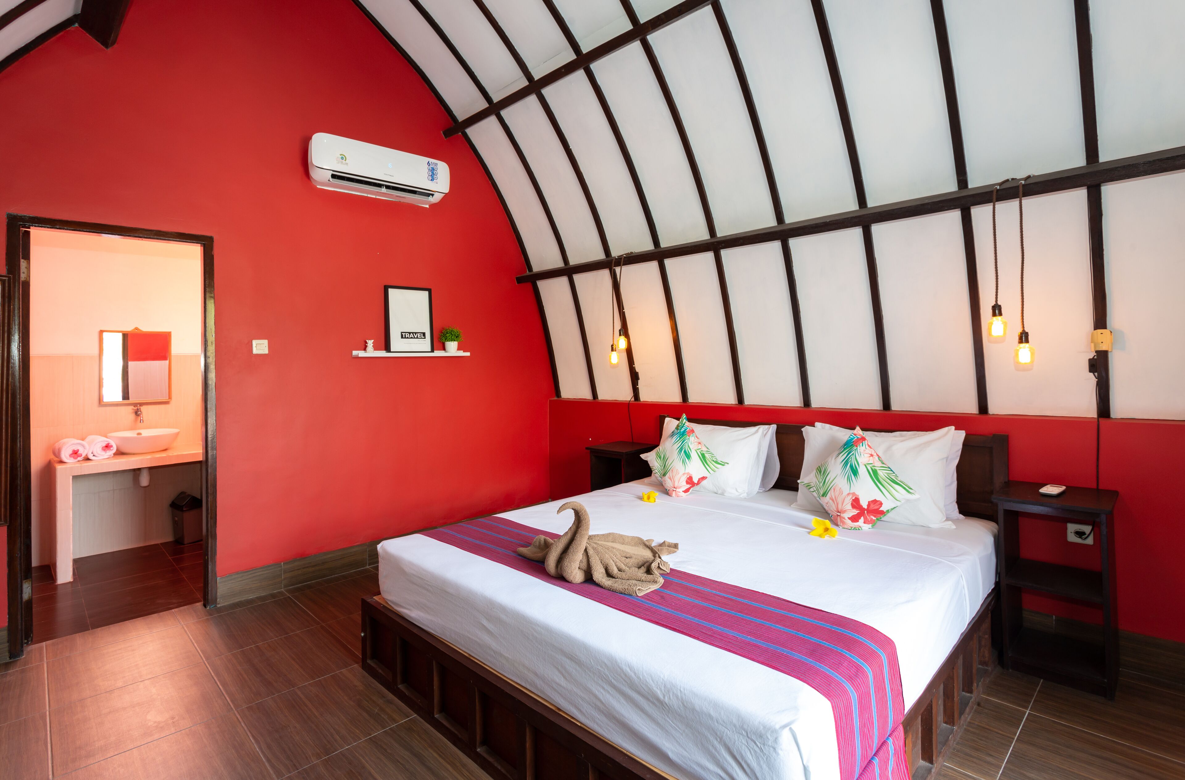 A hotel room with a red wall, a large bed with a white bedspread, a wooden headboard, and a skylight.
