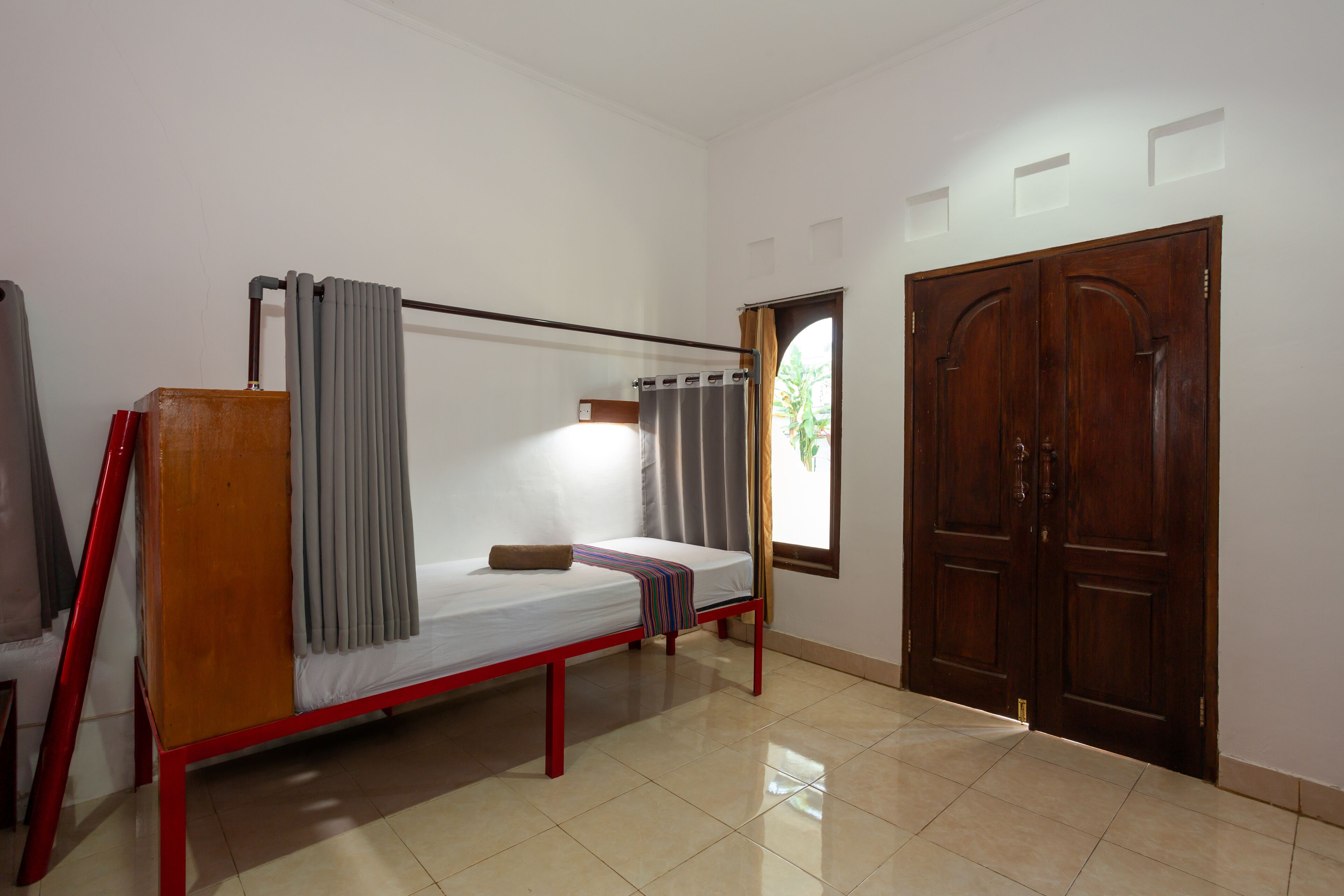 A room with a single bed, a wooden wardrobe, and a window with curtains.