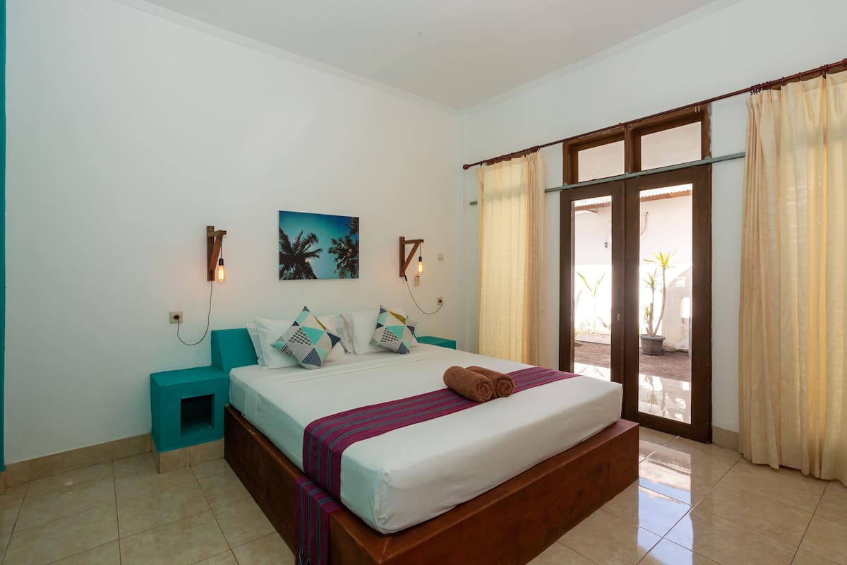 Un dormitorio con cama, mesitas de noche, un cuadro y vistas a través de una puerta corredera.