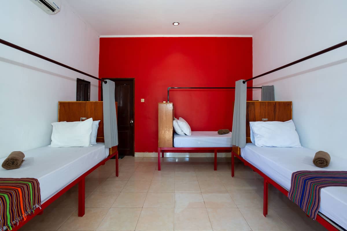 Una habitación con dos camas individuales, un armario de madera y una pared de acento roja.